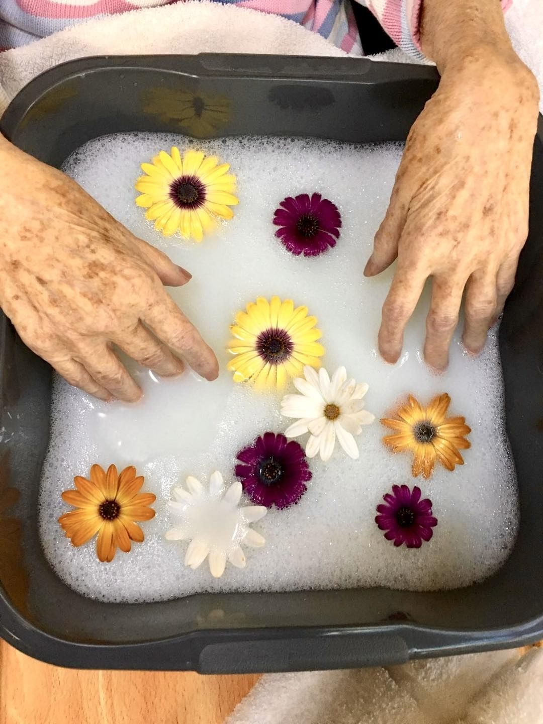 A resident enjoying a warm hand bath scattered with flower heads